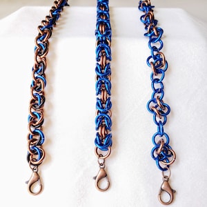 Pode incluir: Três pulseiras feitas de elos de corrente de metal. As pulseiras são azuis e cobre. As pulseiras têm fechos de lagosta.