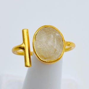 May include: Gold ring with a clear oval-shaped stone and a gold bar design.