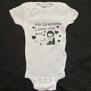 May include: White baby onesie with black text that reads "My Grandma Loves ME and" with a black and white image of Elvis Presley and his signature.