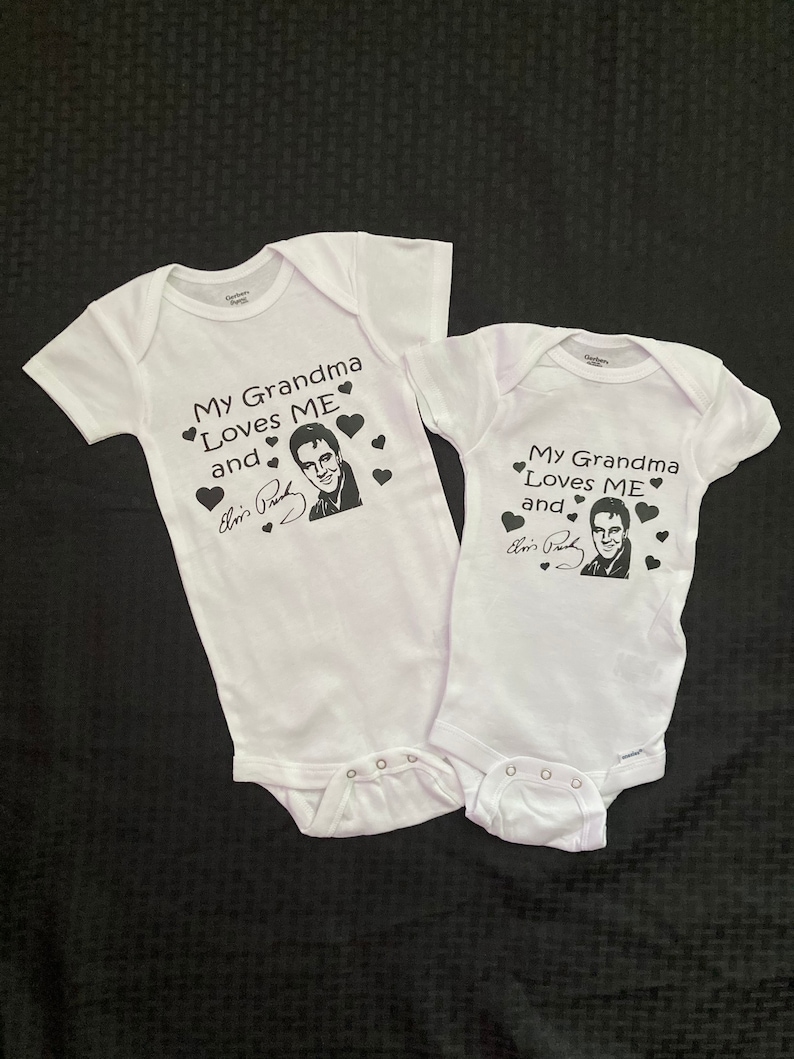 May include: Two white baby onesies with black text that reads "My Grandma Loves Me and" with a picture of Elvis Presley and his signature.