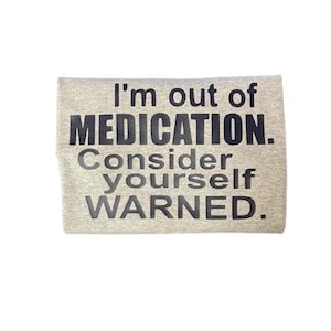 May include: A light gray rectangular item with the text "I'm out of MEDICATION. Consider yourself WARNED." in black, bold letters. The item appears to be a piece of fabric or a similar material.