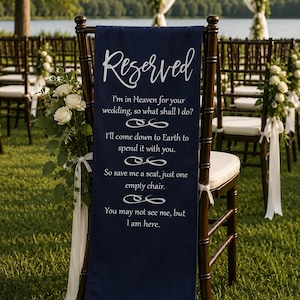 May include: A dark blue "Reserved" sign draped over a wooden chair at an outdoor wedding. The sign has white text with a poem about saving a seat. White flowers and greenery decorate the chairs and arch.