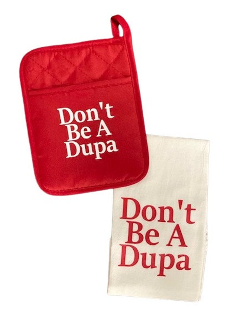 May include: A red quilted potholder with a hanging loop and a white kitchen towel. Both items feature the text Don't Be A Dupa printed in a bold font. The potholder has white text on a red background, while the towel has red text on a white background.