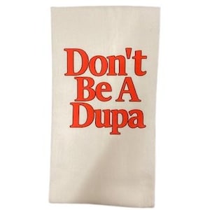 May include: A rectangular off-white kitchen towel featuring the text Don't Be A Dupa printed in a bold, bright orange-red serif font. The fabric has a visible woven texture, and the lettering is centered vertically and horizontally on the towel.