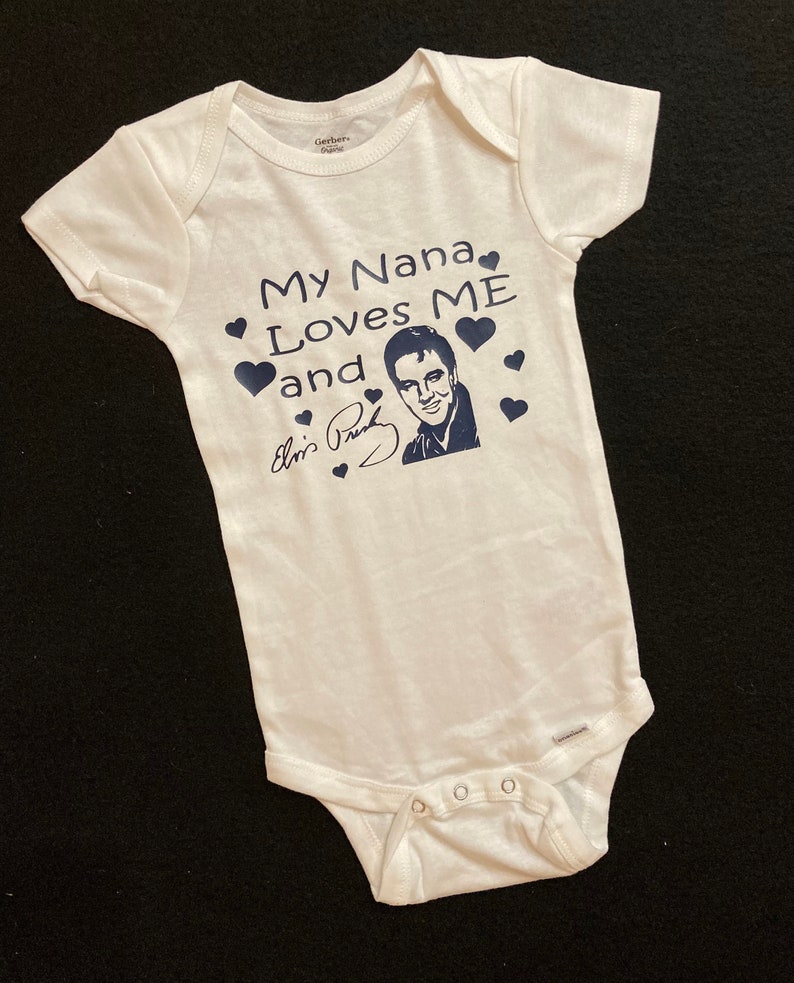 May include: White baby onesie with a blue graphic that says "My Nana Loves Me and Elvis Presley" with a picture of Elvis Presley and a signature.