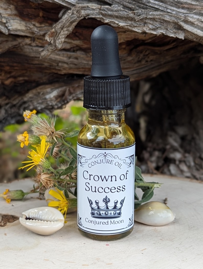 K&ouml;nnte beinhalten: Eine kleine Glasflasche mit schwarzem Tropfer und einem wei&szlig;en Etikett, auf dem "Conjure Oil Crown of Success" mit einer Kronengrafik und "Conjured Moon" unten steht. Die Flasche steht auf einer Holzoberfl&auml;che mit einer Muschel auf jeder Seite.