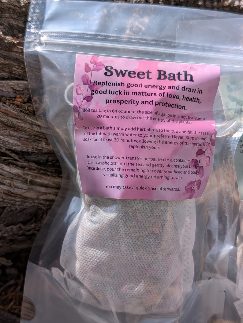 May include: A clear plastic bag containing a tea bag labeled "Sweet Bath." The pink label includes instructions for use and the phrase "Replenish good energy and draw in good luck." The tea bag is white and appears to be filled with herbs.