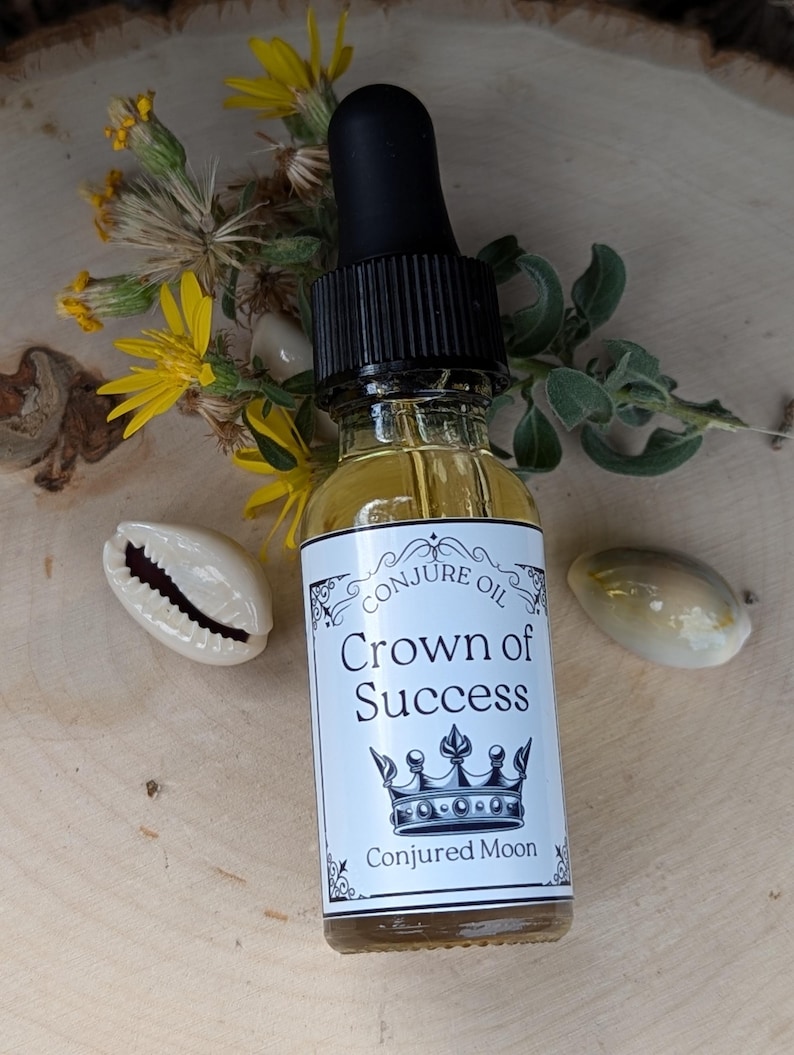 K&ouml;nnte beinhalten: Eine kleine Glasflasche mit schwarzem Tropfer und einem wei&szlig;en Etikett, auf dem "Conjure Oil Crown of Success" mit einer Kronengrafik und "Conjured Moon" unten steht. Die Flasche steht auf einer Holzoberfl&auml;che mit gelben Blumen und Muscheln.
