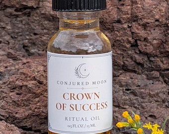 May include: A clear glass bottle with a black ribbed cap containing golden liquid and botanical pieces. The white label reads Conjured Moon, Crown of Success, Ritual Oil, 0.5 fl oz / 15 ml. The bottle is positioned upright.