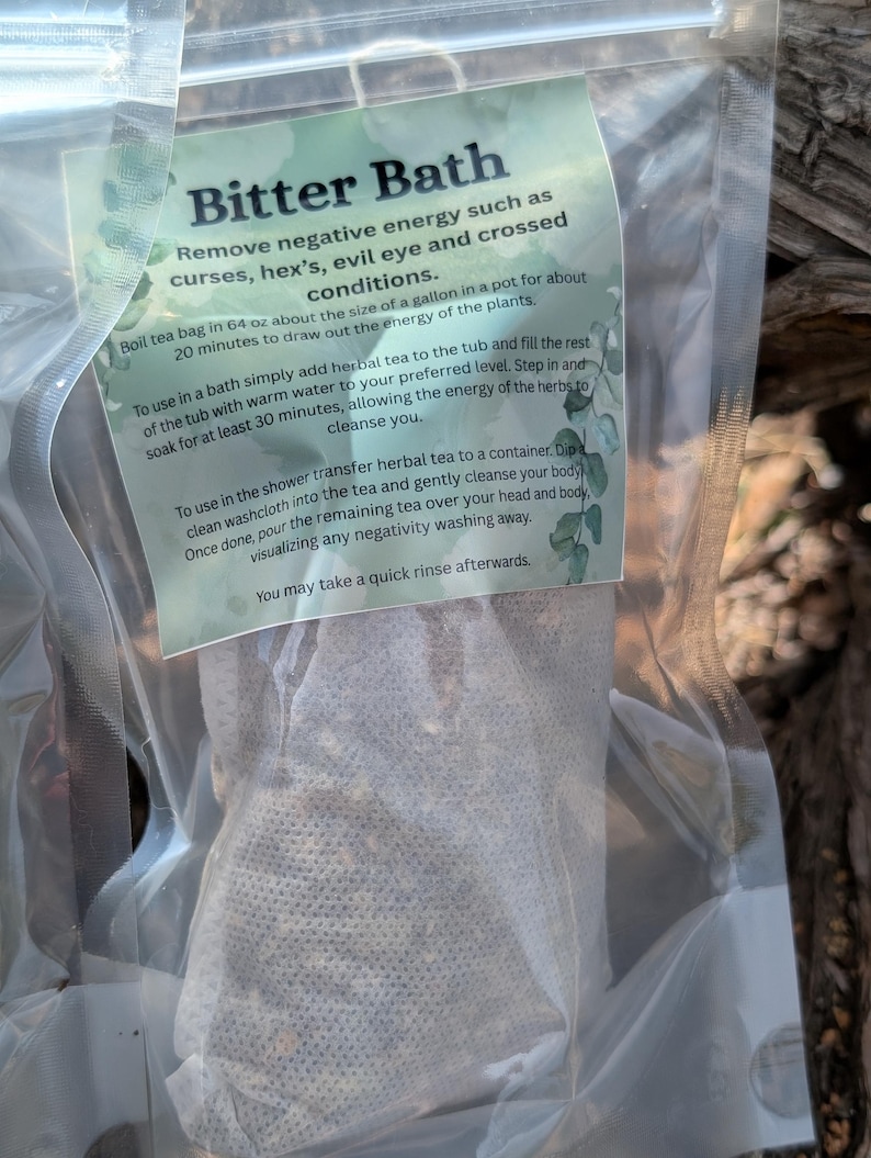 May include: A clear plastic bag containing a tea bag labeled "Bitter Bath." The label, with a green and white design, details instructions for removing negative energy. The tea bag is filled with dried herbs.