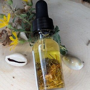 K&ouml;nnte beinhalten: Eine klare Glasflasche mit schwarzem Tropfer, gef&uuml;llt mit einer gelben Fl&uuml;ssigkeit und getrockneten Kr&auml;utern und Blumen. Die Flasche steht auf einer Holzoberfl&auml;che.