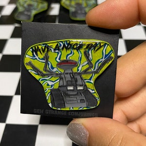 May include: A yellow, blue, and white enamel pin featuring a robot with the text "Have a Nice Day" and "Sew Strange Conjurings".