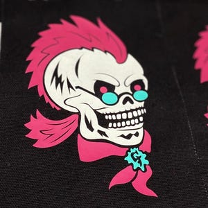 Könnte beinhalten: Schwarze Stoffaufnäher mit einem Totenkopf-Design. Der Totenkopf hat einen pinkfarbenen Irokesenschnitt, türkisfarbene Brille und einen pinkfarbenen Schal. Der weiße Schädel hat einen detaillierten Kiefer. Der Text "SEWSTRANGECONJURINGS" steht unten. Die Aufnäher liegen auf einer schwarz-weiß karierten Oberfläche.