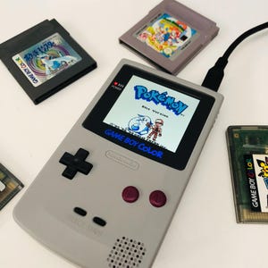 Puede incluir: Una taza de cerámica blanca con un asa negra y el texto "But First, Coffee" en negro y negrita. La taza está sobre una superficie blanca. La taza mide aproximadamente 10 cm de alto.