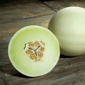 May include: A halved cantaloupe melon with visible seeds on a wooden surface. The melon is light green and has a smooth skin. The other half of the melon is whole and sits next to the halved melon.