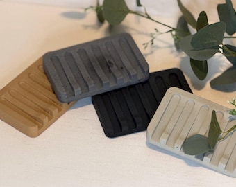 May include: A set of four rectangular soap dishes in tan, dark gray, black, and light beige. Each dish features a series of parallel raised ridges designed for drainage, with a smooth, solid construction and a matte finish throughout.