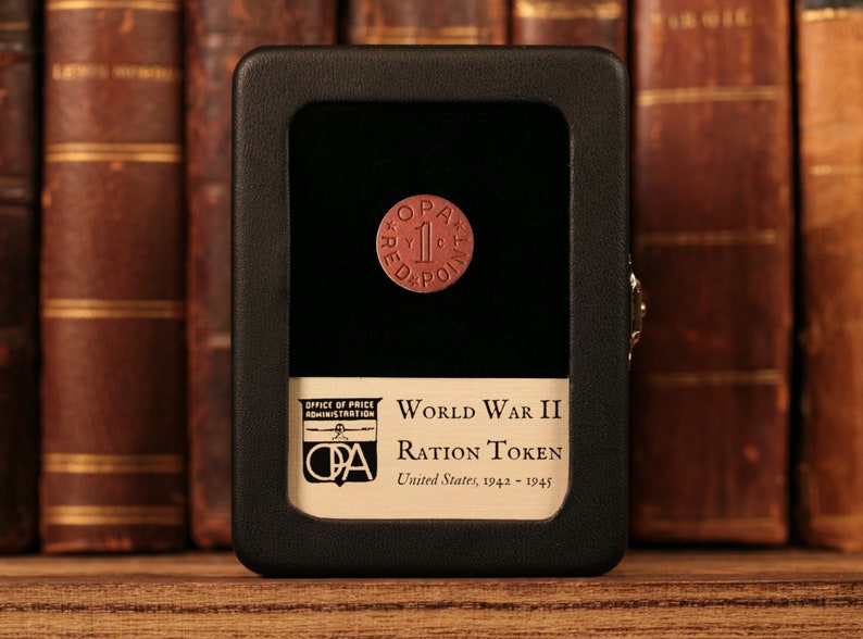 May include: A red World War II ration token with the text "OPA 1 RED POINT" in a black display case. The case has a label that reads "OFFICE OF PRICE ADMINISTRATION WORLD WAR II RATION TOKEN United States, 1942-1945".