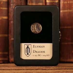 May include: A bronze coin in a black display case with a white label that reads "Elymais Drachm c. 147 BC - 224 AD".