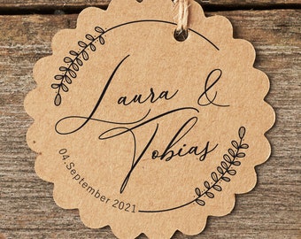 Könnte beinhalten: Ein brauner, gewellter, runder Stempel mit dem Text "Laura & Tobias" und "04. September 2021" in schwarzer Schrift. Der Stempel ist von einem Kranz aus Blättern umgeben.