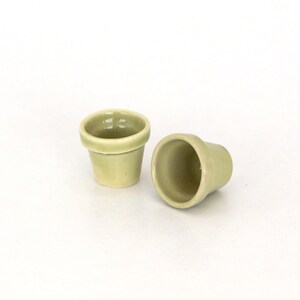 May include: Two small, light green ceramic flower pots. One pot is upright, the other is laying on its side.