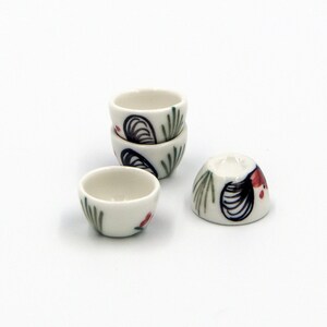 Op de afbeelding: Vier kleine witte keramische kommen met een bloemenmotief. De kommen zijn in een piramidevorm gestapeld, met de bovenste kom lichtjes naar de zijkant gekanteld.