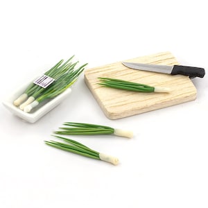 Puede incluir: Cebolletas verdes en miniatura con bases blancas dispuestas sobre una superficie blanca. También hay una pequeña tabla de cortar de madera con un cuchillo plateado y unas cebolletas. Un plato rectangular blanco contiene un manojo de cebolletas.