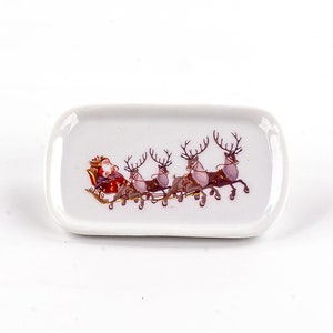 May include: White ceramic rectangular tray with a Christmas scene of Santa Claus in a sleigh pulled by four reindeer.