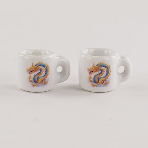 Puede incluir: Dos tazas de cerámica blanca con un diseño de dragón azul y dorado.