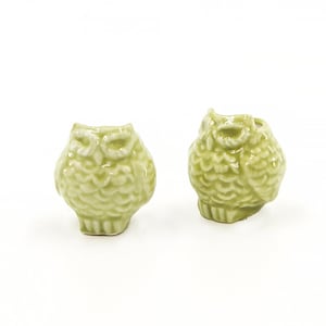 May include: Two small ceramic owl figurines in a light green color. The owls are facing forward with their wings folded.