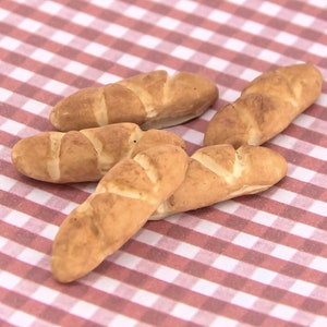 May include: Four small, brown, crusty bread rolls on a red and white checkered tablecloth.