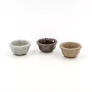 May include: Three small ceramic bowls in different colors. The bowls are white, brown, and beige.