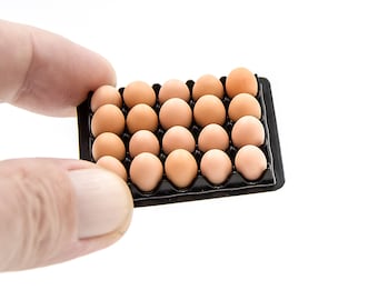 May include: A black plastic egg carton filled with brown eggs. The carton is being held by a hand.
