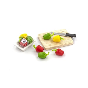 May include: A miniature kitchen set with a wooden cutting board, a silver knife, and a white plate with a package of red peppers, yellow peppers, and green peppers.