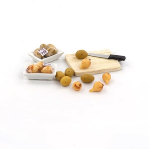 Puede incluir: Una escena de cocina en miniatura con una tabla de cortar blanca, un cuchillo y una variedad de patatas en miniatura de color amarillo y verde. Las patatas están en dos cuencos blancos y en la tabla de cortar.
