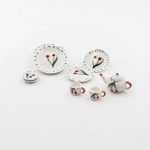 Puede incluir: Un juego de té en miniatura con una tetera blanca, tazas y platillos decorados con cerezas rojas y hojas verdes. Perfecto para casas de muñecas o juegos en miniatura.