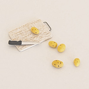 May include: A white cutting board with a brown and white pattern, a black handled knife, and four yellow potatoes with brown spots.