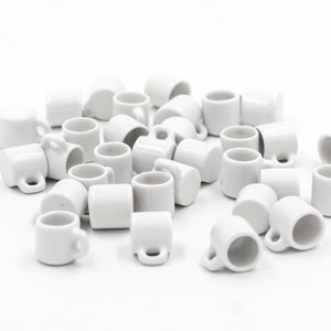Puede incluir: Una colección de 30 tazas de cerámica blanca en miniatura. Las tazas son todas del mismo tamaño y forma, y están dispuestas en una pila sobre una superficie blanca.