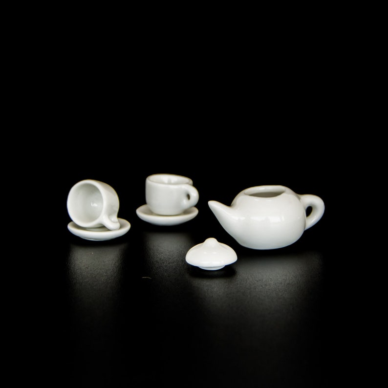 May include: A white porcelain tea set with a teapot, two cups, and two saucers. The set is on a black background.