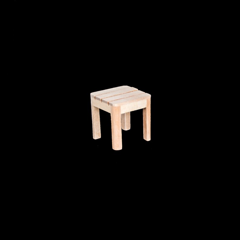 Puede incluir: Un peque&ntilde;o taburete de madera con un acabado marr&oacute;n claro. El taburete tiene una parte superior cuadrada y cuatro patas.
