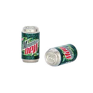 May include: Two miniature Mountain Dew soda cans. One can is upright, the other is on its side. The cans are green with the Mountain Dew logo in red and white. The cans have silver tops and bottoms.