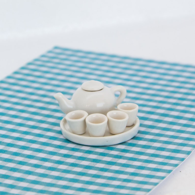 May include: A miniature white ceramic tea set, including a teapot with a lid and three small cups on a matching tray. The set is placed on a blue and white checkered surface, suggesting a playful or decorative theme.