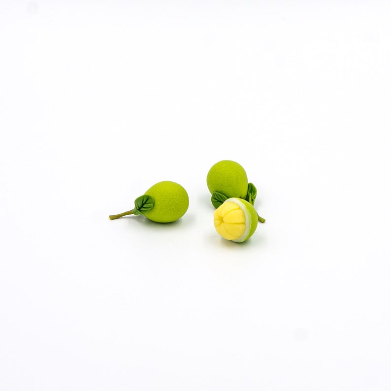 May include: Three small green fruit with leaves, one is cut open to reveal a yellow interior.