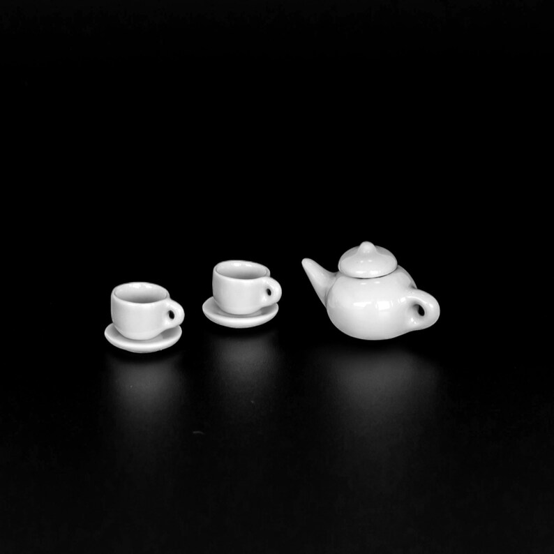 May include: A white teapot and two white teacups with saucers on a black background.