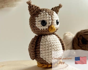 Op de afbeelding: Gehaakt amigurumi speelgoed in de vorm van een uil, gemaakt van bruin en wit garen. De uil heeft grote zwarte ogen en een gele snavel. Het speelgoed staat op een houten oppervlak. Haakpatroon PDF.