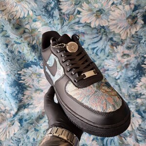 May include: Black leather low-top sneakers with a floral pattern on the upper. The laces are black and the shoe has a white swoosh logo on the side.