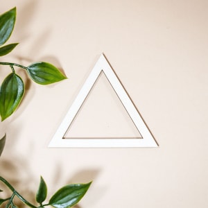 Pode incluir: Um quadro triangular branco sobre um fundo bege com folhas verdes no canto.
