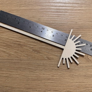 Può includere: Un progetto di artigianato in legno con un design a forma di sole. Il sole ha 16 raggi e un diametro di 15 cm. Un righello viene utilizzato per misurare il sole.