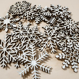 May include: A collection of wooden snowflake ornaments in various sizes and shapes. The snowflakes are made of light brown wood and have a delicate, intricate design.