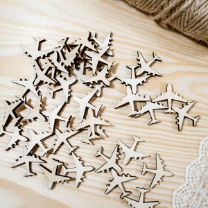 May include: A pile of wooden airplane cutouts on a light brown wooden surface. The cutouts are in various sizes and are arranged in a random pattern.