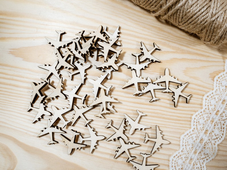 May include: A pile of wooden airplane cutouts on a light brown wooden surface. The cutouts are in various sizes and are arranged in a random pattern.